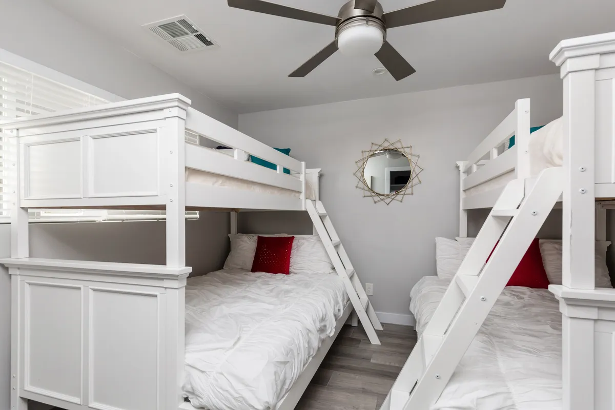 A playful bunk room with sturdy bunk beds, a large mirror, and a ceiling fan. The cozy layout is designed for shared experiences, encouraging games, reading, and bonding before bedtime—perfect for kids or groups of friends.
