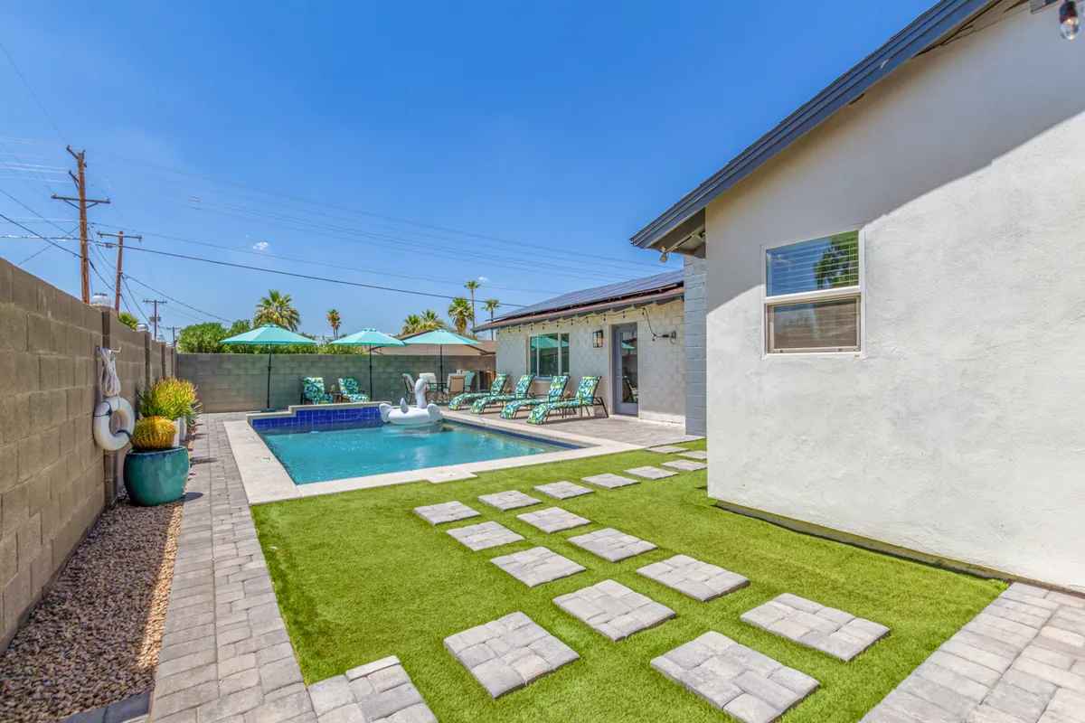 A serene backyard scene with a sparkling swimming pool surrounded by lounge chairs and decorative umbrellas, set along a stone pathway. The atmosphere is relaxed, inviting, and perfect for unwinding after a day of exploration.