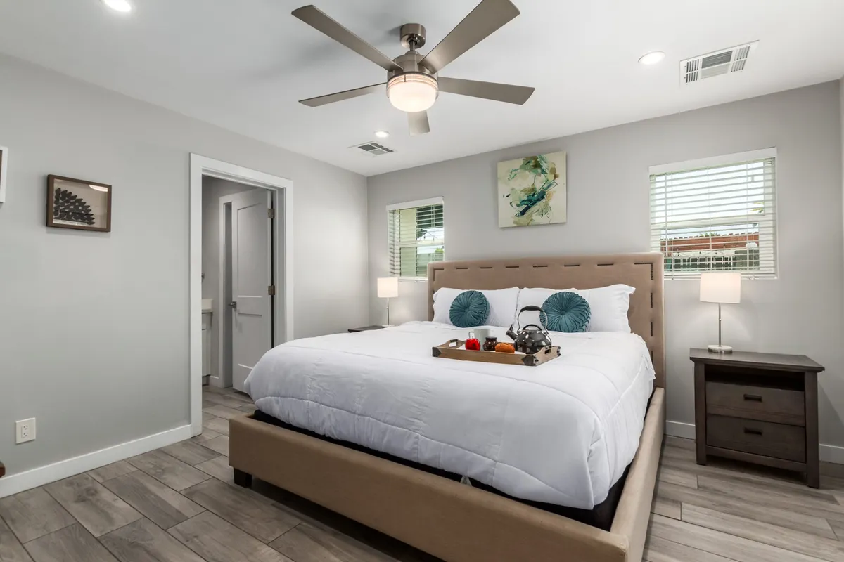 A serene bedroom with a neatly made bed adorned with decorative pillows, a breakfast tray resting atop the blankets, tasteful wall art above the headboard, and a cozy nightstand with a lamp. The soft light and thoughtful touches evoke a welcoming and restful retreat, representative of a king suite.