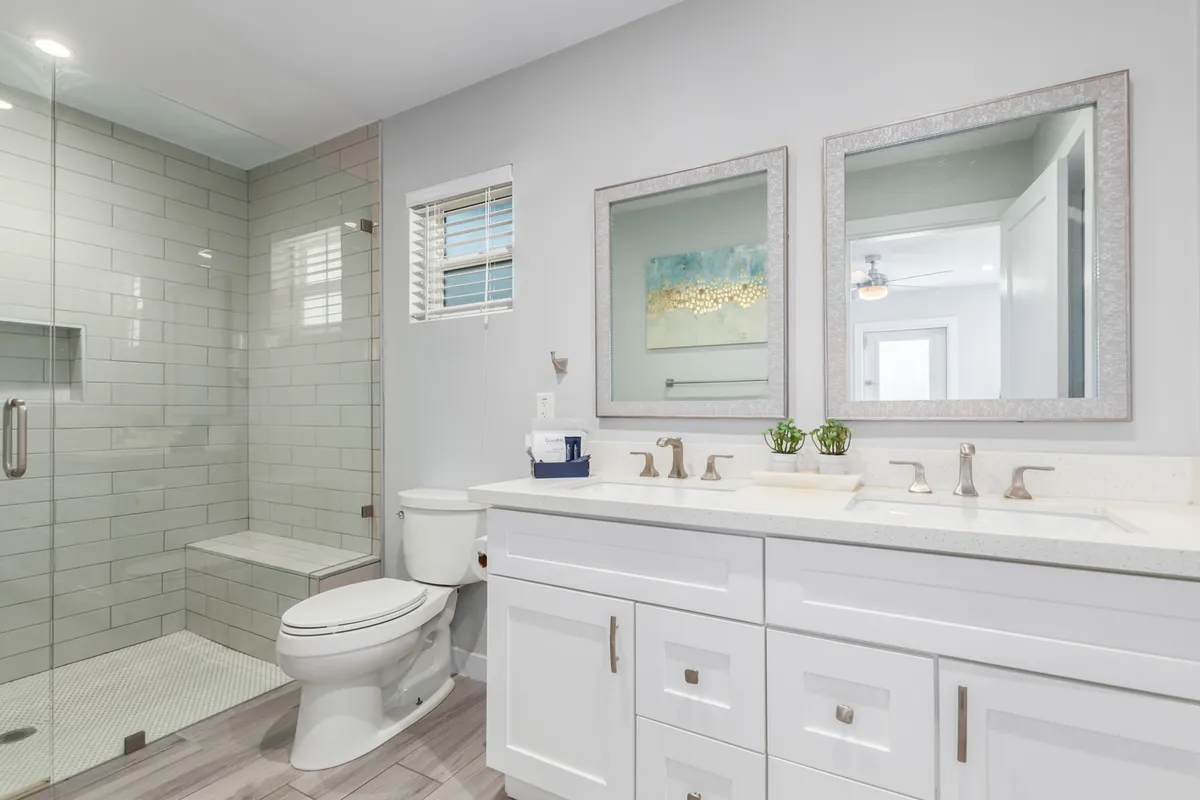 A modern, spa-inspired bathroom featuring a double sink vanity, a glass shower enclosure, and mirrored frames. The fresh design encourages rejuvenation and relaxation, echoing the resort-style amenities and thoughtful starter kits described in the section.