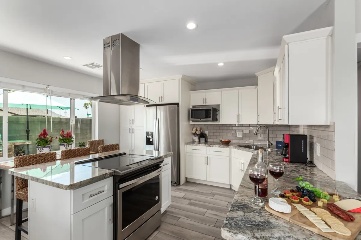 An island kitchen scene with a contemporary countertop set for hosting, including wine glasses and a food platter, and sleek modern appliances in the background. The setup conveys a space made for entertaining and casual dining, capturing the spirit of togetherness.