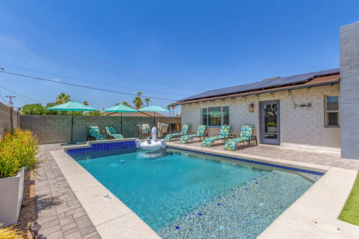 A sparkling swimming pool framed by lounge chairs, umbrellas, and a vibrant pool float. The area is surrounded by lush greenery, suggesting a serene and private space for sunbathing, swimming, and poolside relaxation.